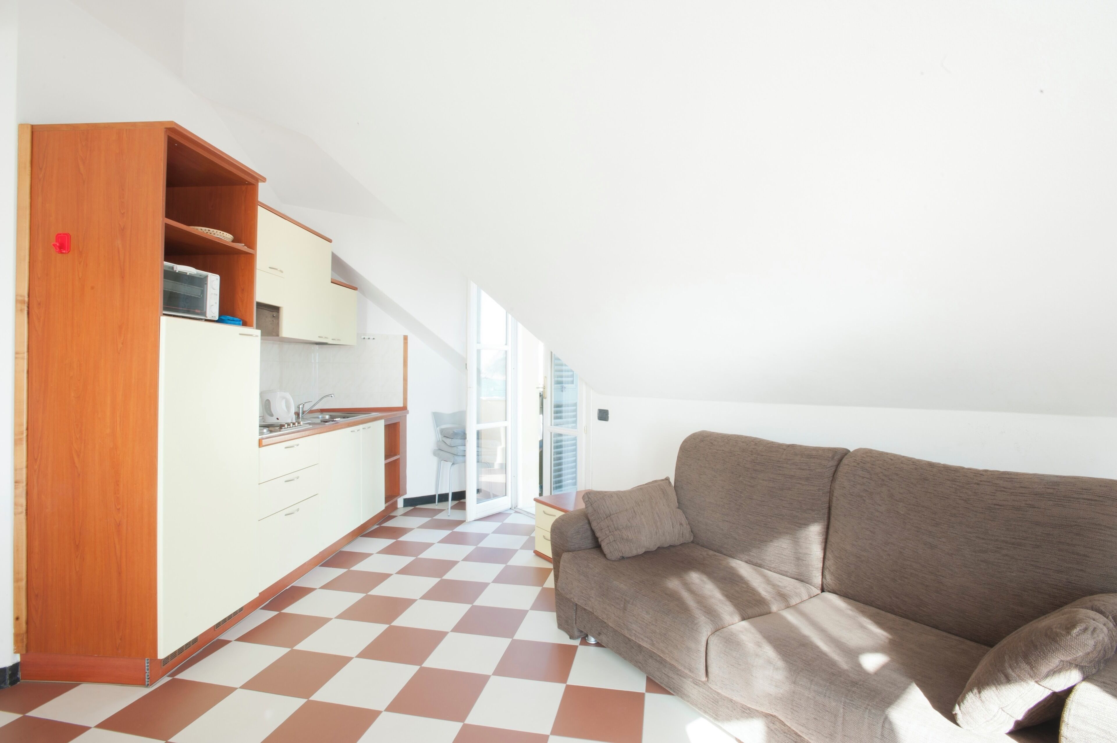 Una cocina moderna con armarios blancos y piso a cuadros, un sofá marrón y un ventanal corredizo que da a un balcón.