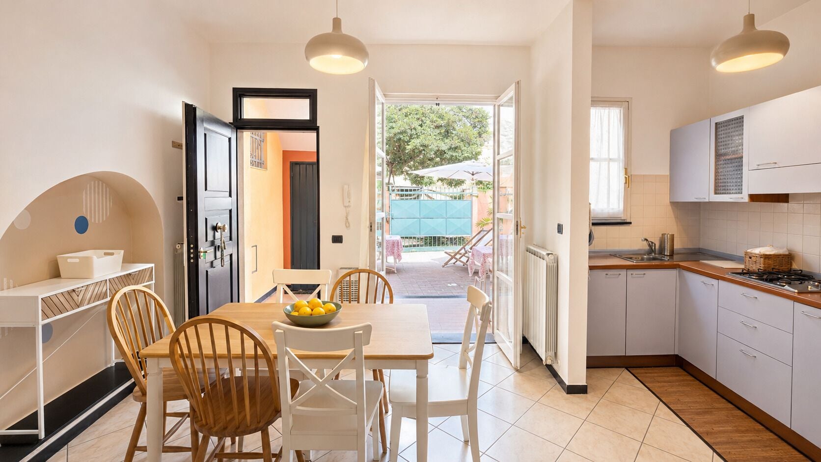 A modern kitchen with white cabinets, a dining table with chairs, and a view to an outdoor patio.