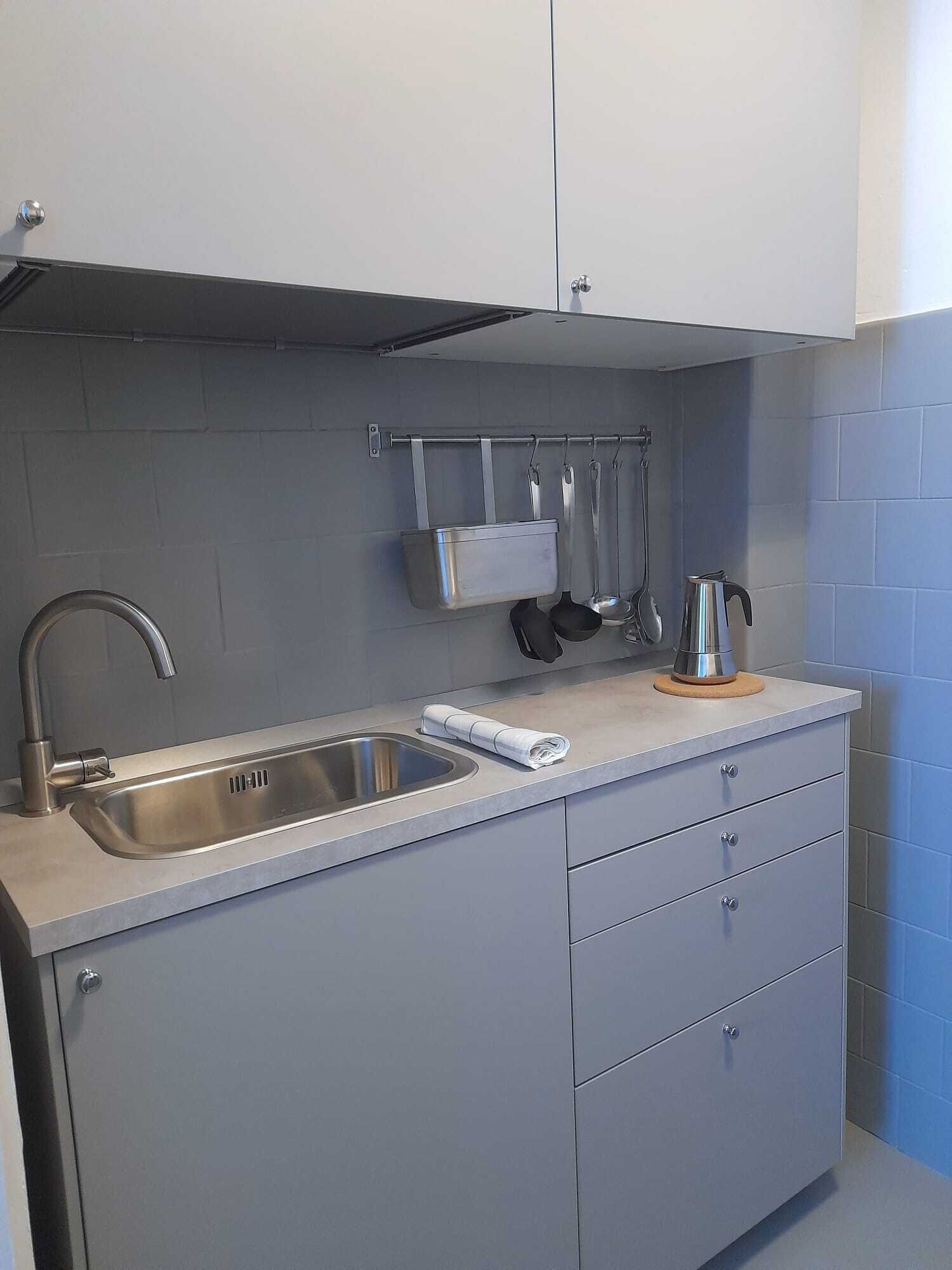 A compact kitchen with a stainless steel sink, a kettle, and a knife block.