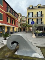 A street with colorful buildings, a pedestrian crossing sign, and a large metallic sculpture.