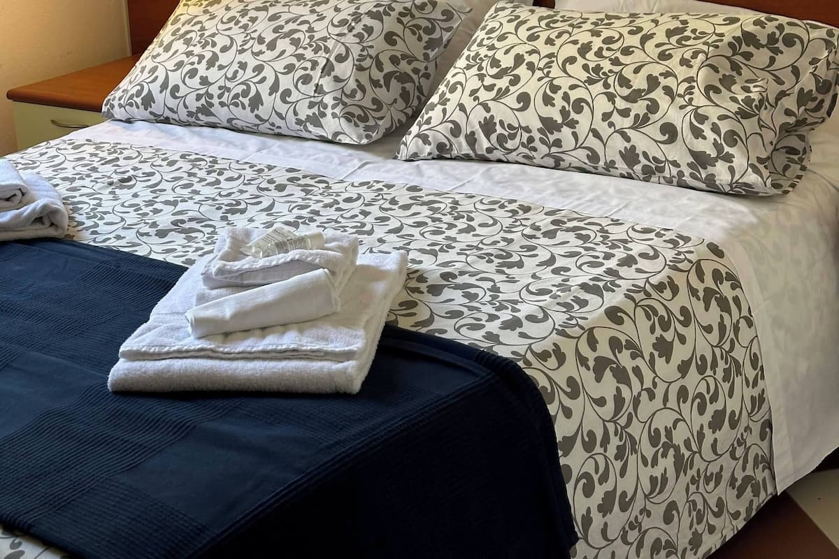 A neatly made bed with patterned bedding, a bedside lamp, and a folded towel on the nightstand.
