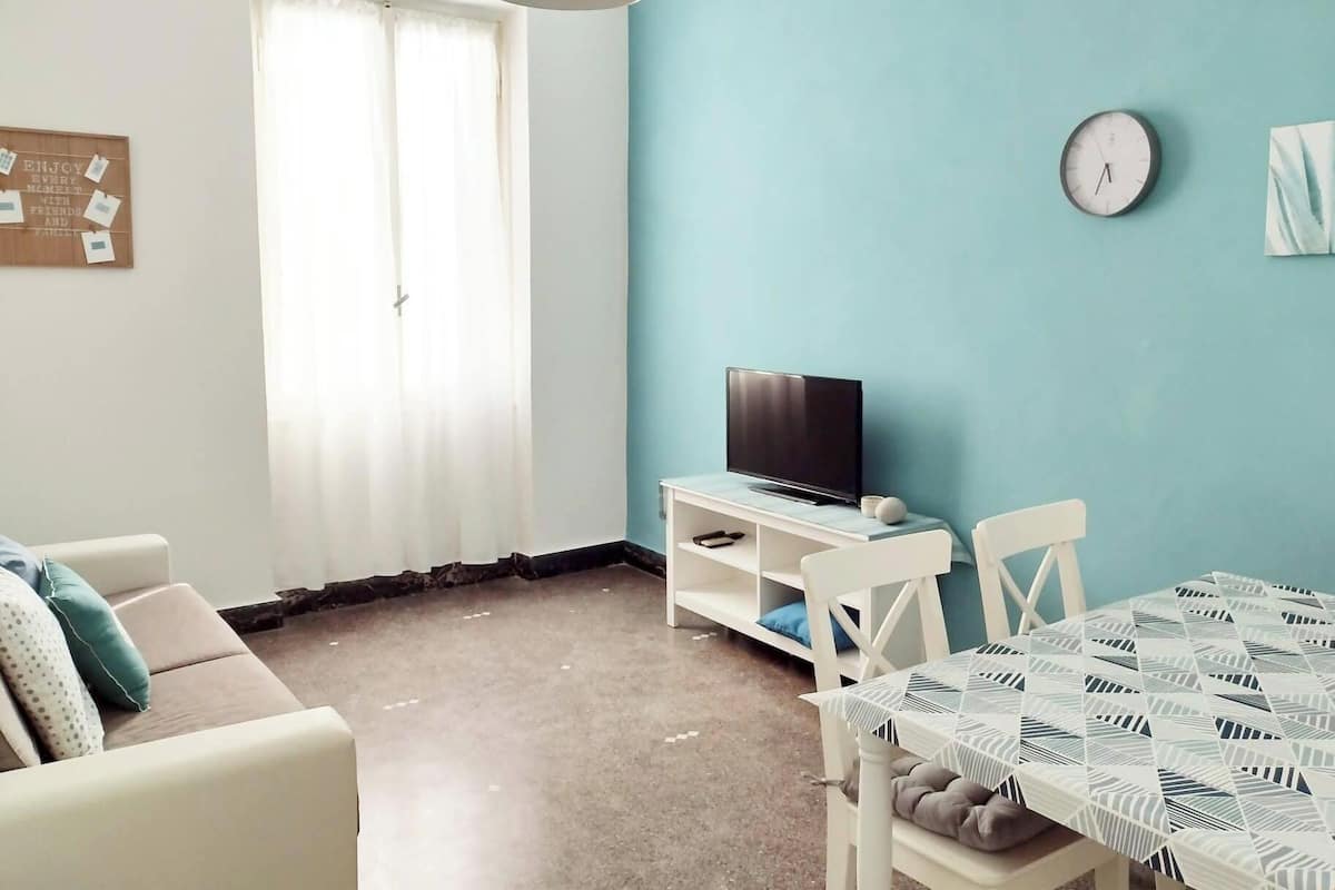 A living room with a TV, a dining table, and a clock on the wall.