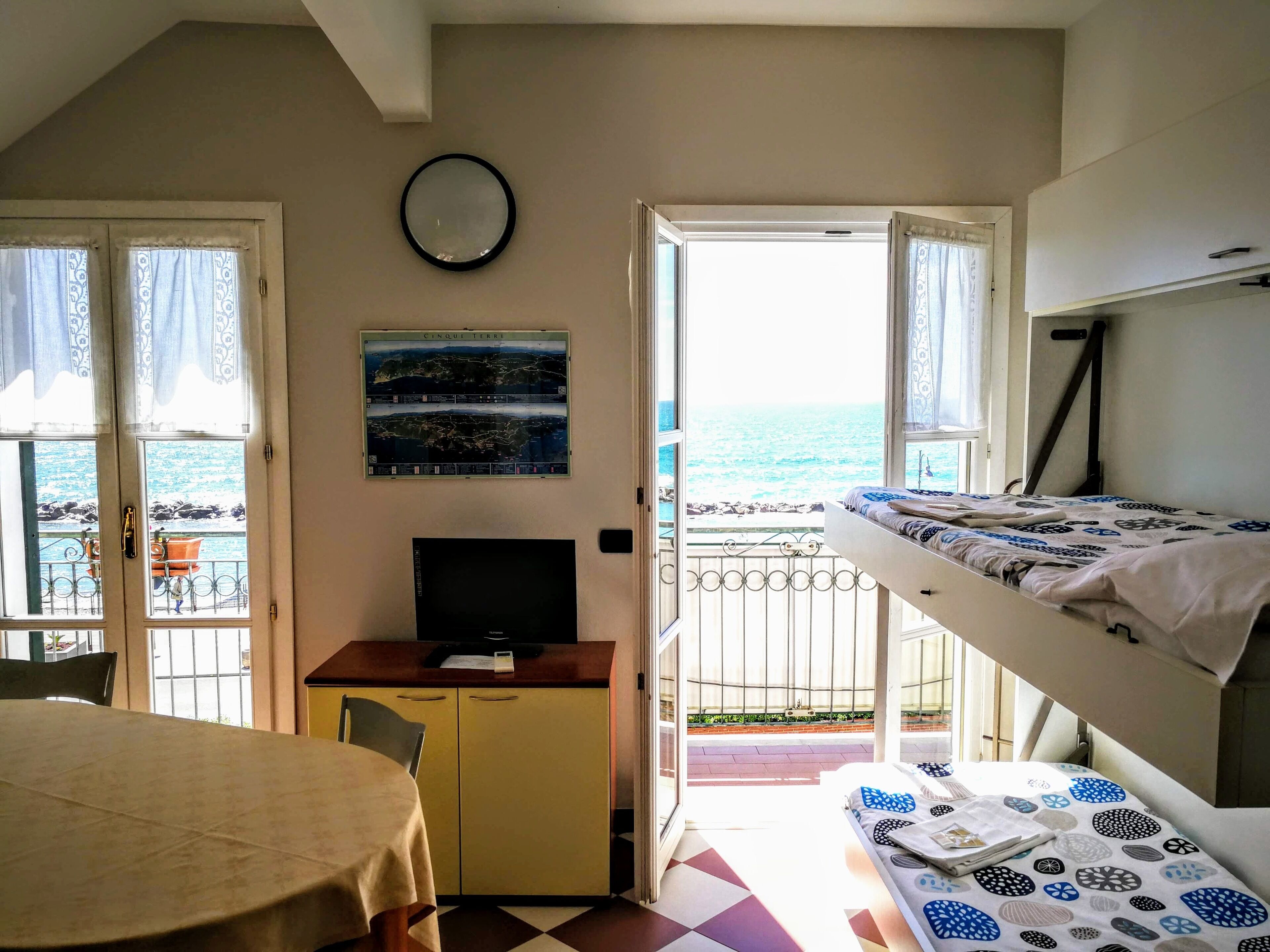 A room with a bed, a desk, a chair, a television, and a view of the sea.