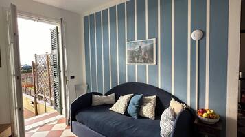 A living room with a blue sofa, patterned cushions, a framed picture on the wall, and a bowl of fruit on a side table.