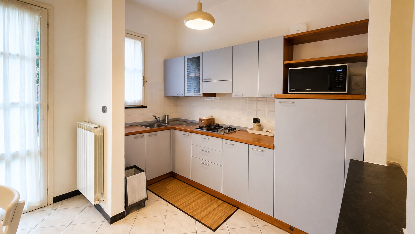 A compact kitchen with white cabinets, a microwave, a stove, and a radiator.