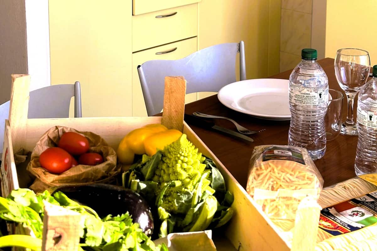 A kitchen with yellow cabinets, a stove, and a sink. There is a table with a plate, a bottle, and a glass.