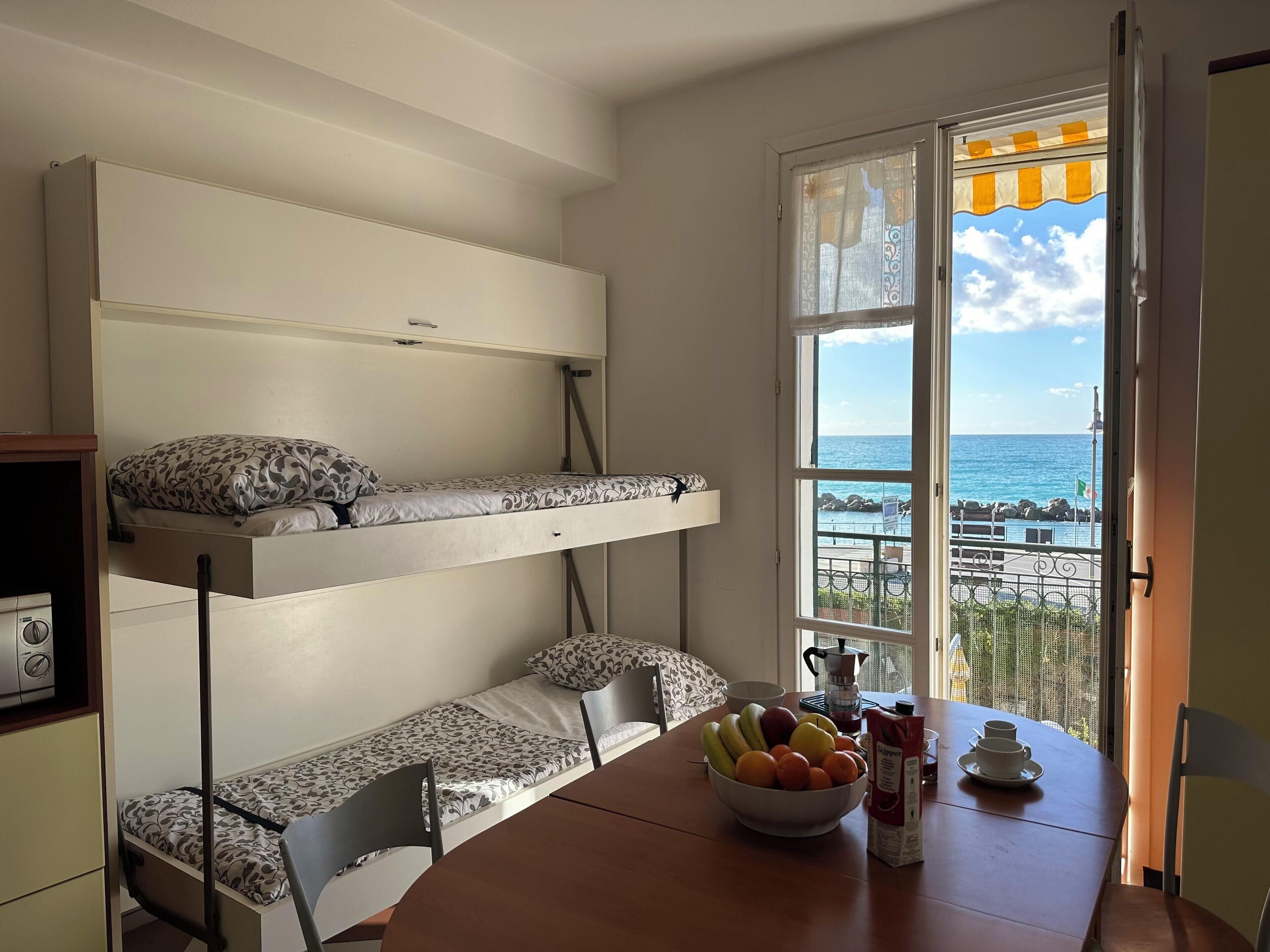 Une chambre avec un lit superposé, une table à manger avec des fruits et une vue sur la mer.