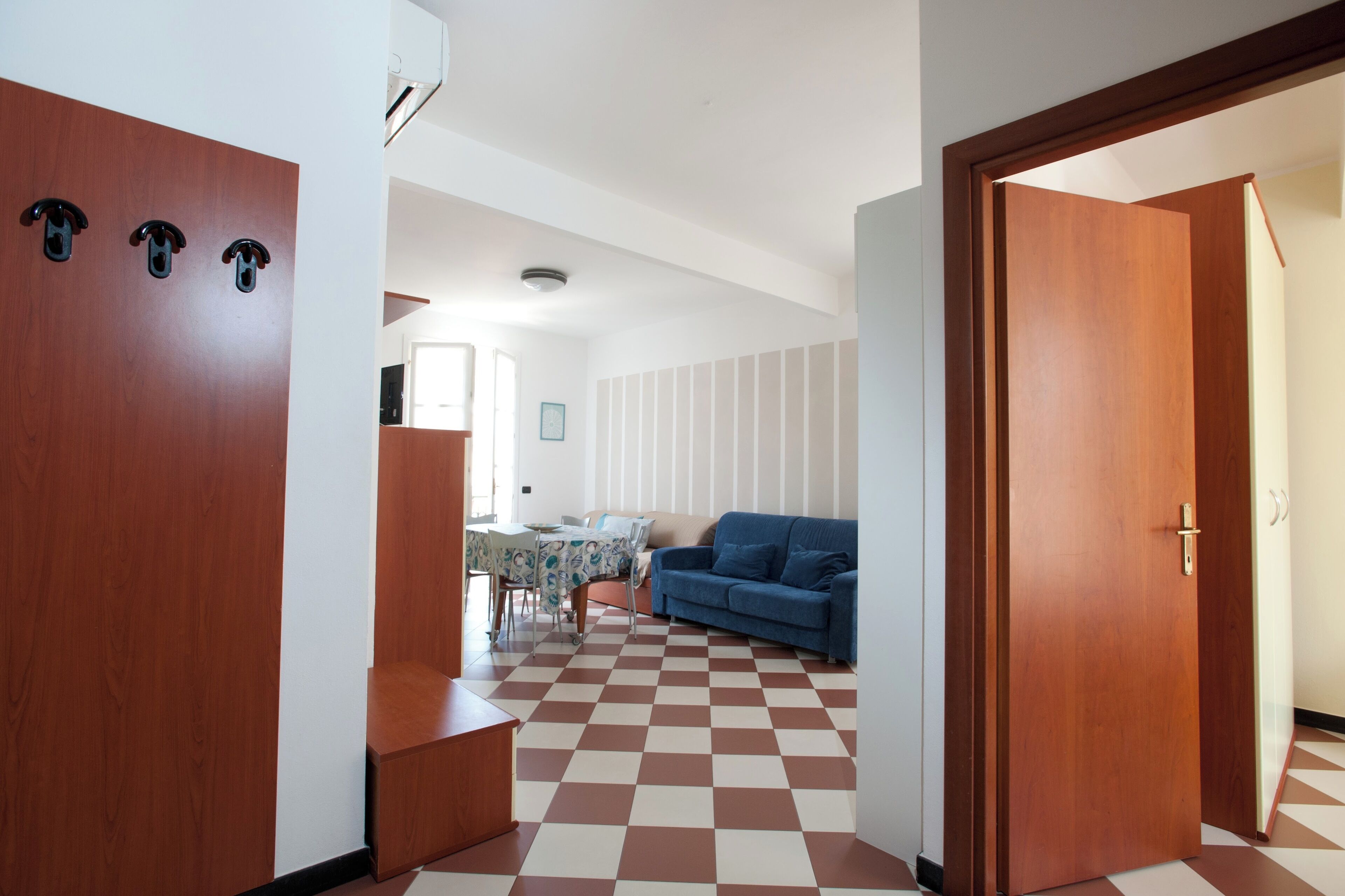 Una stanza con pavimento a scacchi, un divano blu, un tavolo da pranzo con sedie e porte in legno.