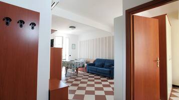 Una stanza con pavimento a scacchi, un divano blu, un tavolo da pranzo con sedie e porte in legno.