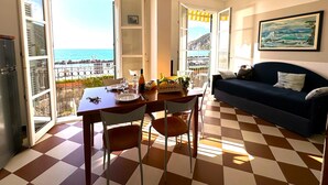 A room with a checkered floor, a dining table with chairs, a sofa, and a view of the sea through open doors. - Giada Residence (Moneglia)