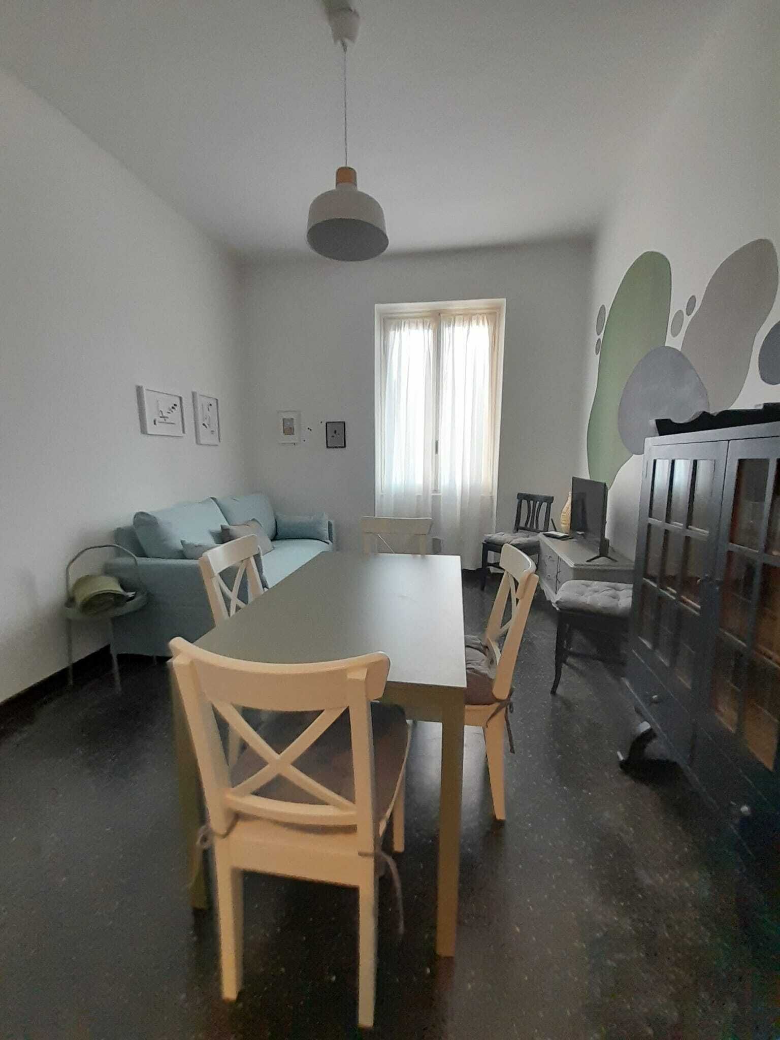 Un coin repas comprenant une table et des chaises, un canapé, une fenêtre avec des rideaux et un mur orné d’œuvres d’art abstraites.