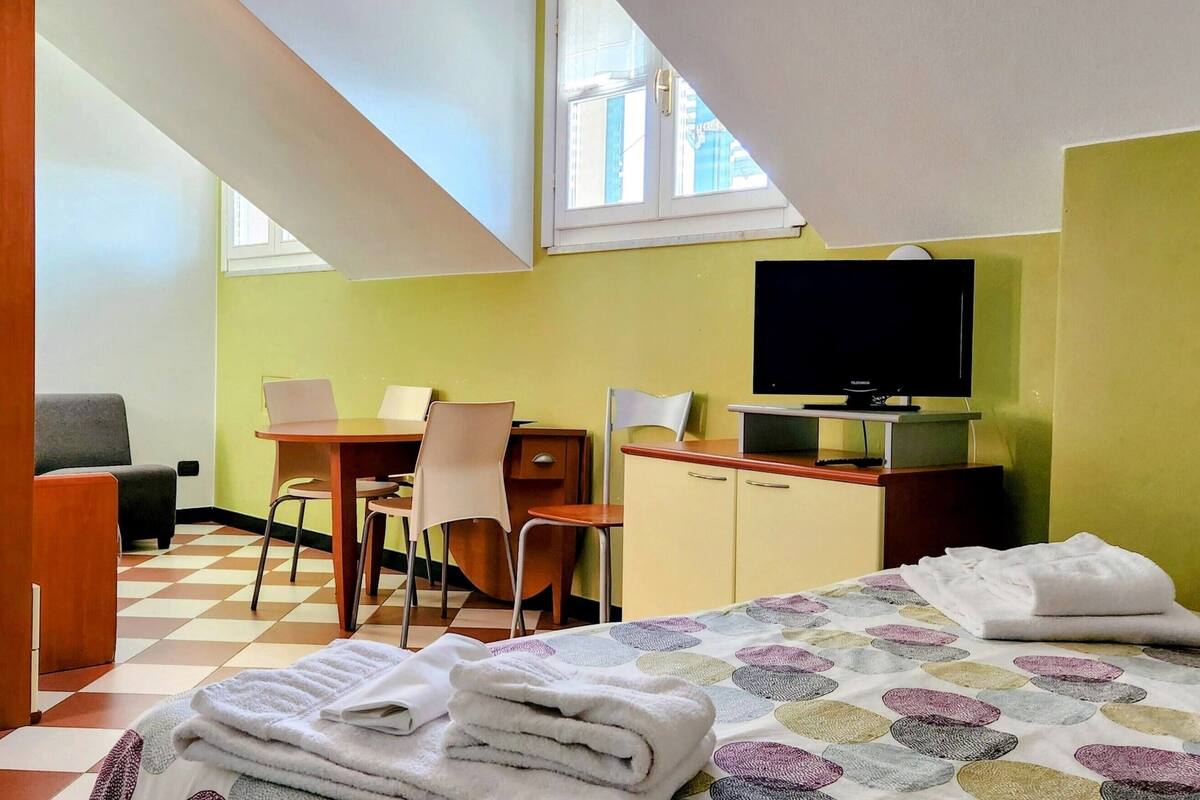 A hotel room with a bed, a desk, a chair, a television, and a window.