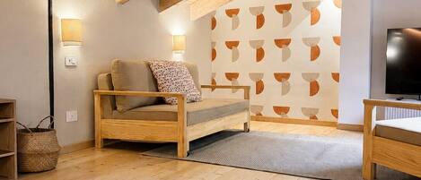 Une chambre à coucher confortable, aménagée dans un grenier avec des poutres apparentes, comprenant un lit, un téléviseur et un mur décoré d’un motif.