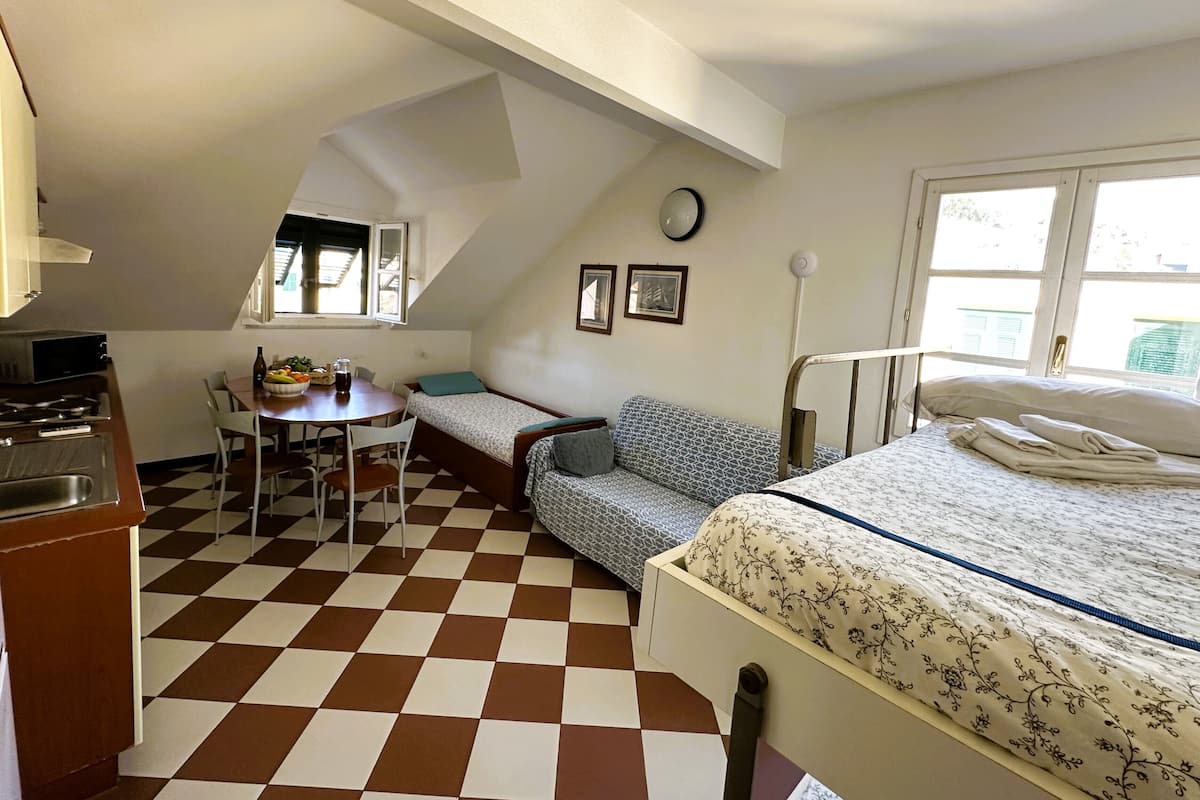A compact room with a kitchenette, a dining area, a bed, and a window providing natural light.