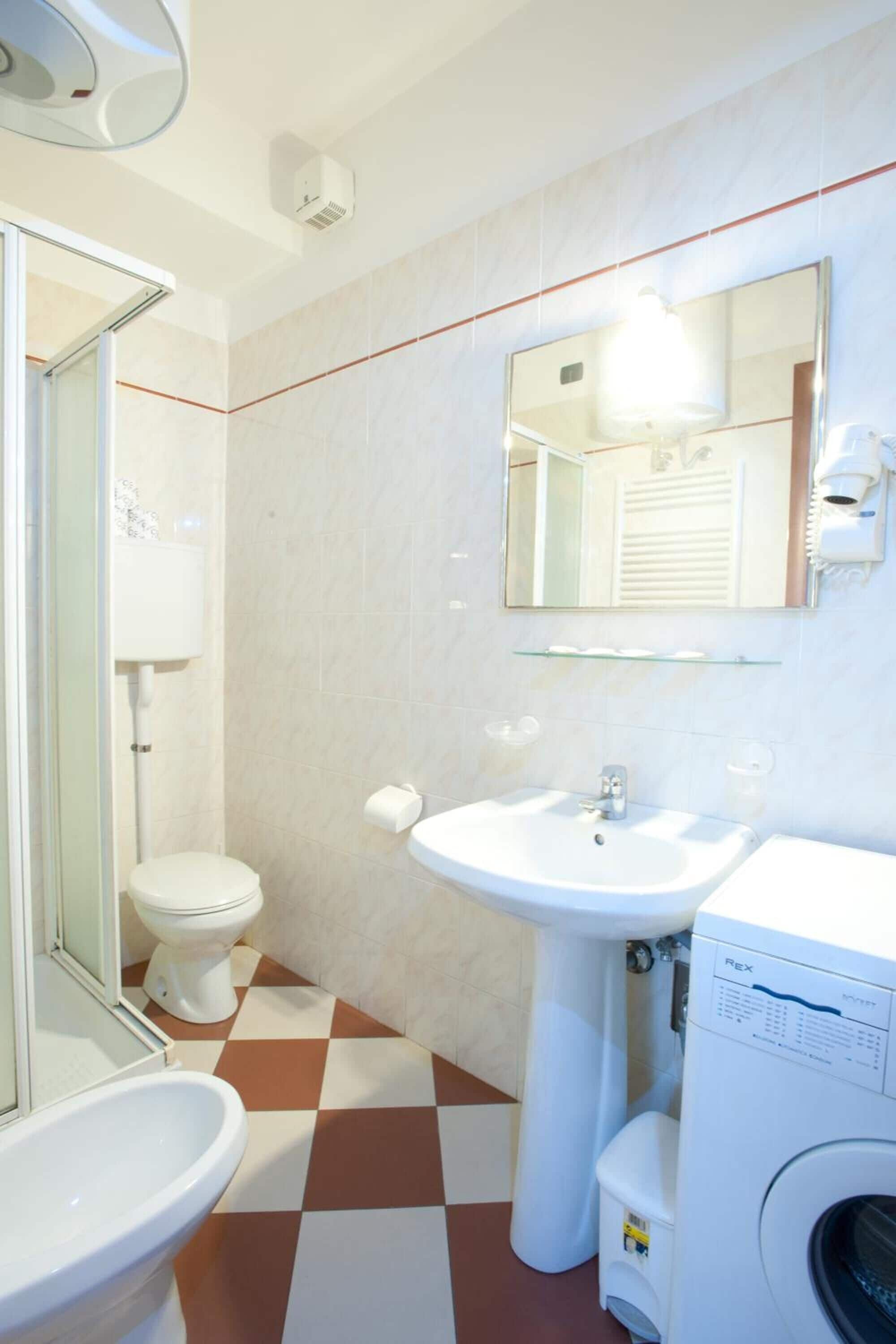 A bathroom with a checkered floor, a sink, a toilet, and a washing machine.
