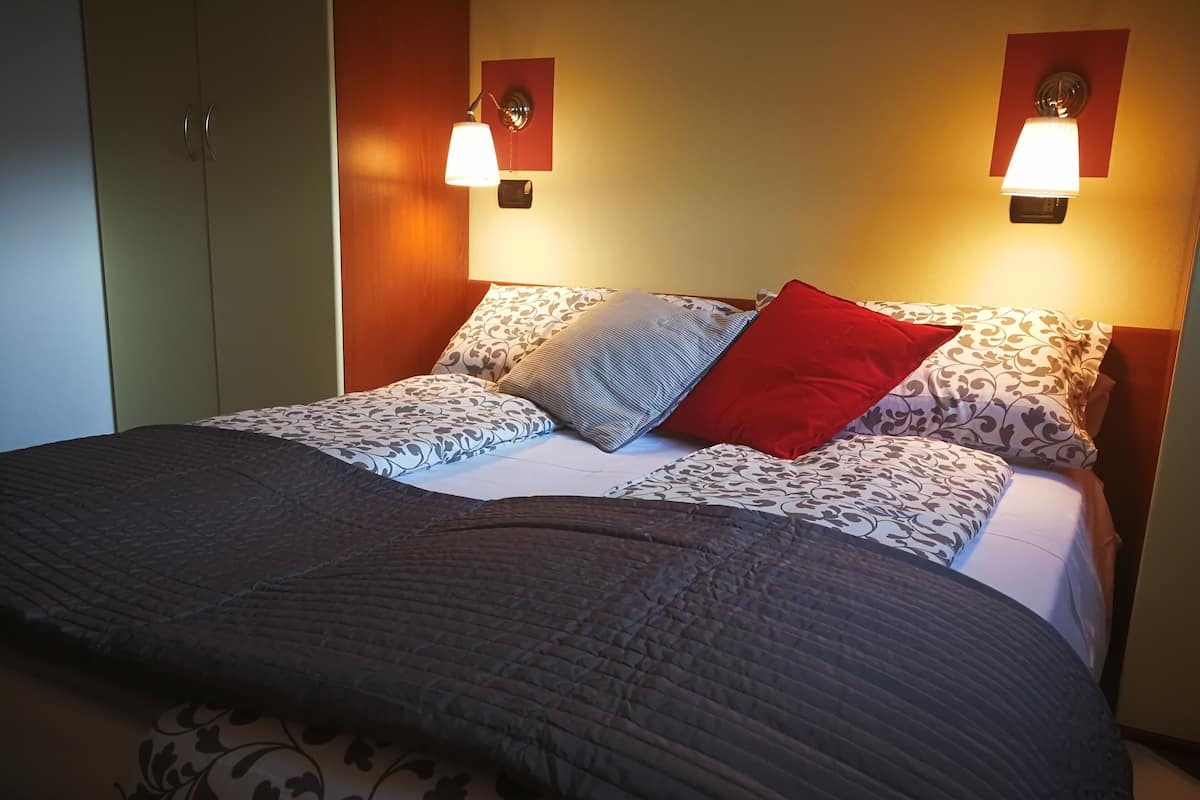 A neatly made bed with patterned bedding and a dark quilt, flanked by two wall-mounted lamps.