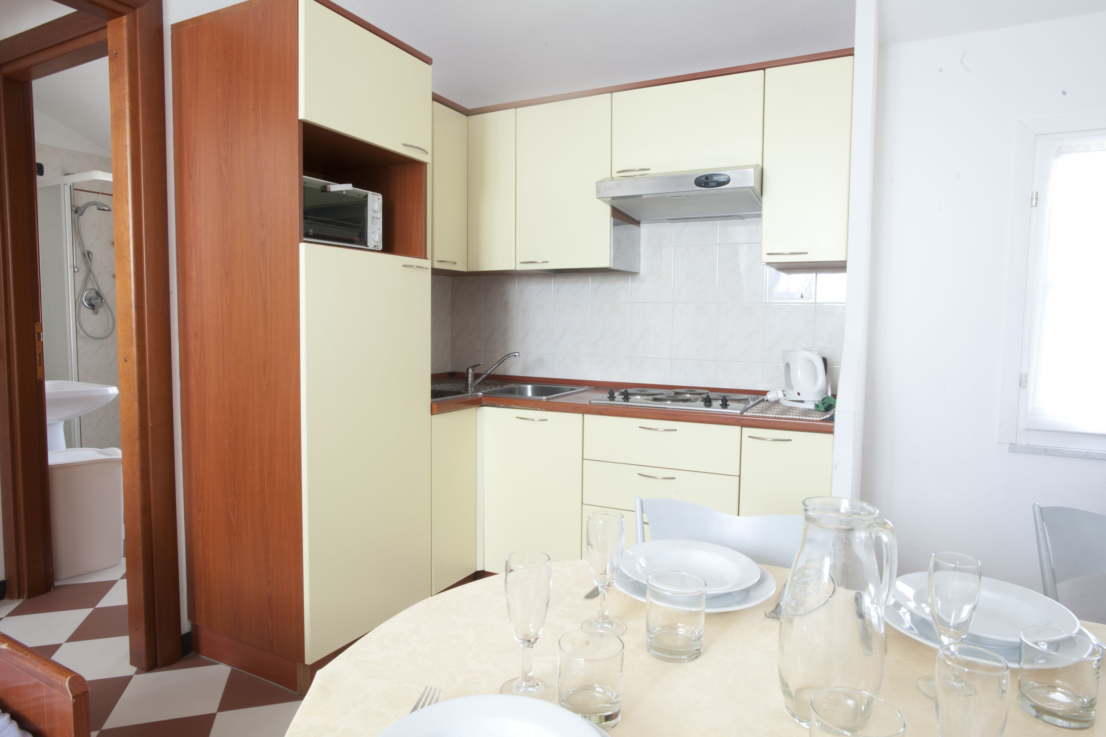 A compact kitchen with a sink, stove, and cabinets. There is a dining table set with plates and glasses.