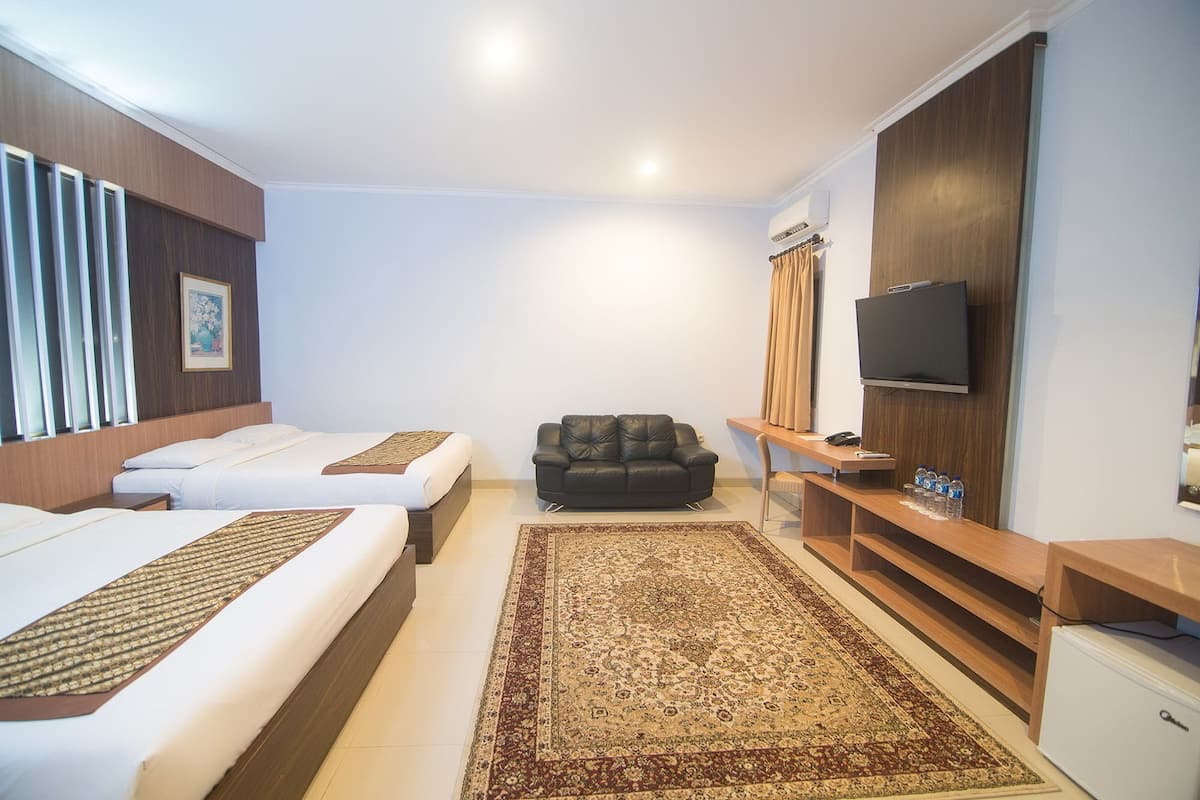 A hotel room with two single beds, a sofa, a television, and a minibar.