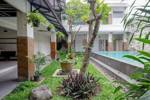 A modern indoor pool area with a stone wall, potted plants, and a tree. - Dinasty Smart Hotel (Surakarta)