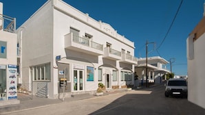 A white hotel with balconies, an ATM, and a sign for a nearby restaurant. - Meltemi Hotel (Milos)