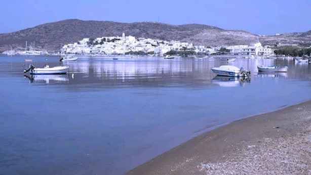 A coastal town with boats on calm waters, a sandy beach, and a hill in the background. - Meltemi Hotel (Milos)