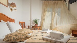 A hotel room with a bed, a nightstand, a lamp, a potted plant, and a window with curtains. - Meltemi Hotel (Milos)