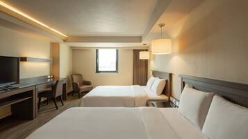 A hotel room with two beds, a desk with a TV, a chair, and a window with curtains.