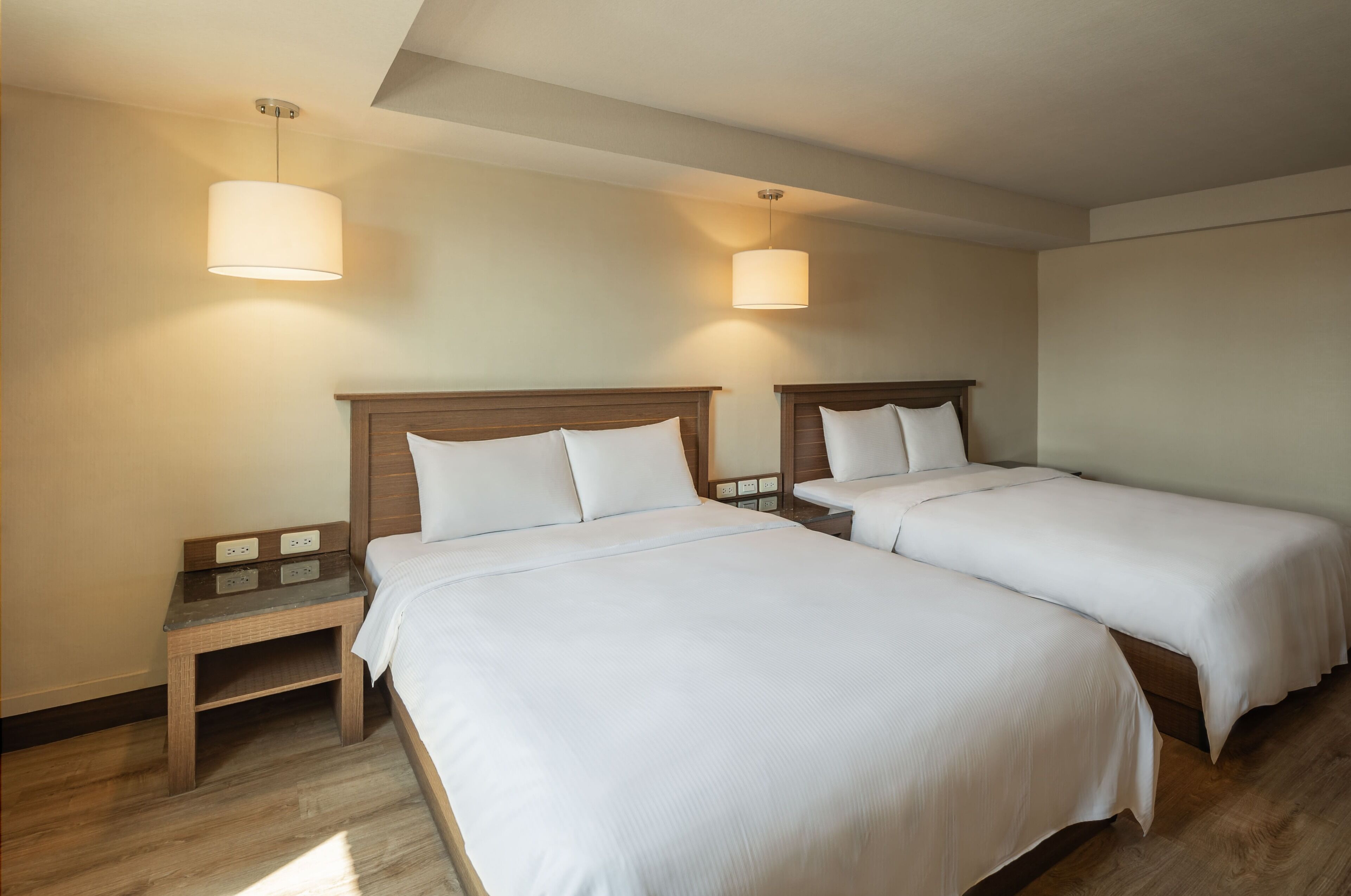 A hotel room with two single beds, a nightstand, and a small table.