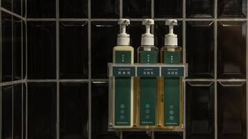 A bathroom shelf with three bottles of shampoo, conditioner, and body wash from Kindness Hotel.
