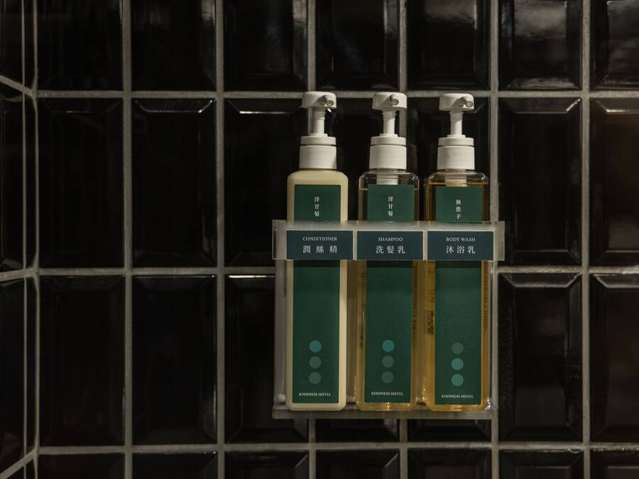 A bathroom shelf with three bottles of shampoo, conditioner, and body wash from Kindness Hotel.