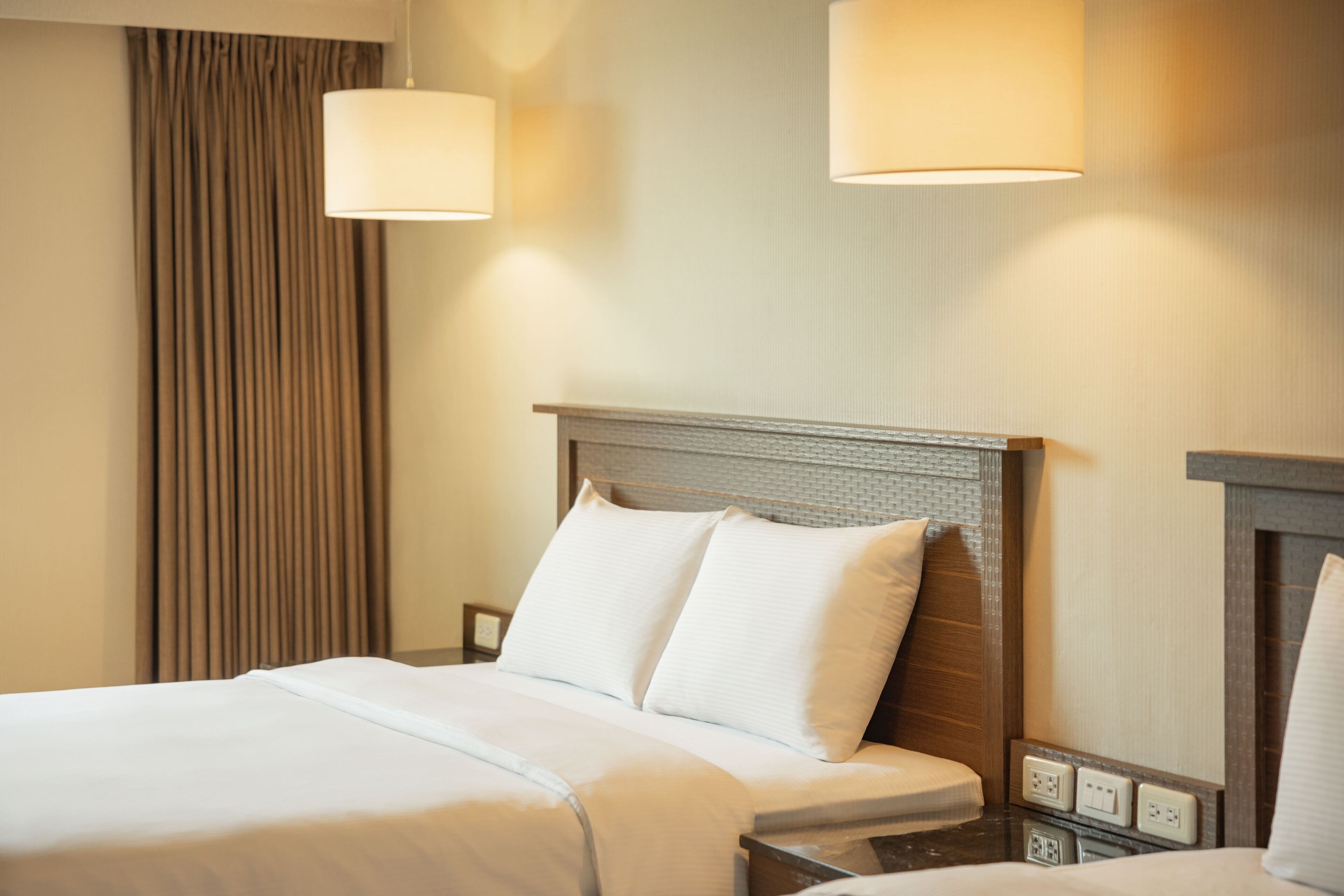 A hotel room with a neatly made bed, a headboard with a textured design, and two wall-mounted lamps.