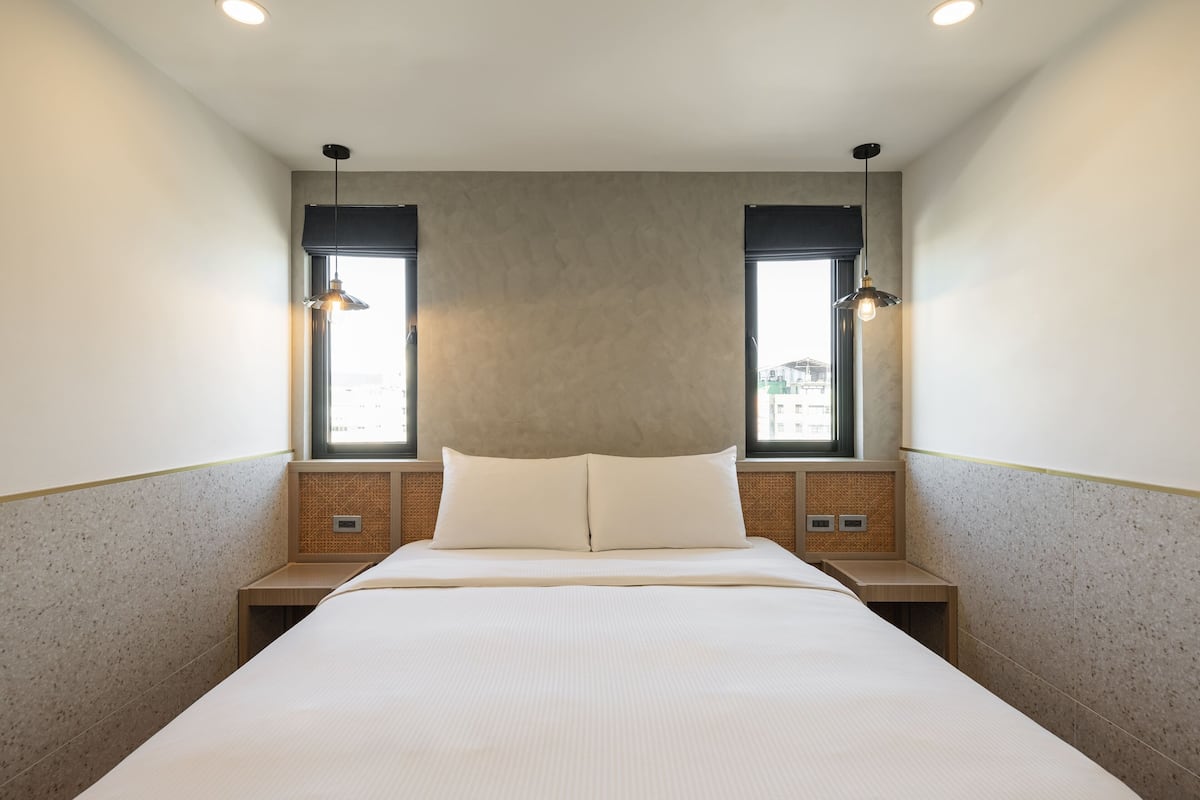Ein modernes Hotelzimmer mit einem großen Bett, zwei Nachttischen und einem Kopfteil mit integrierter Beleuchtung.