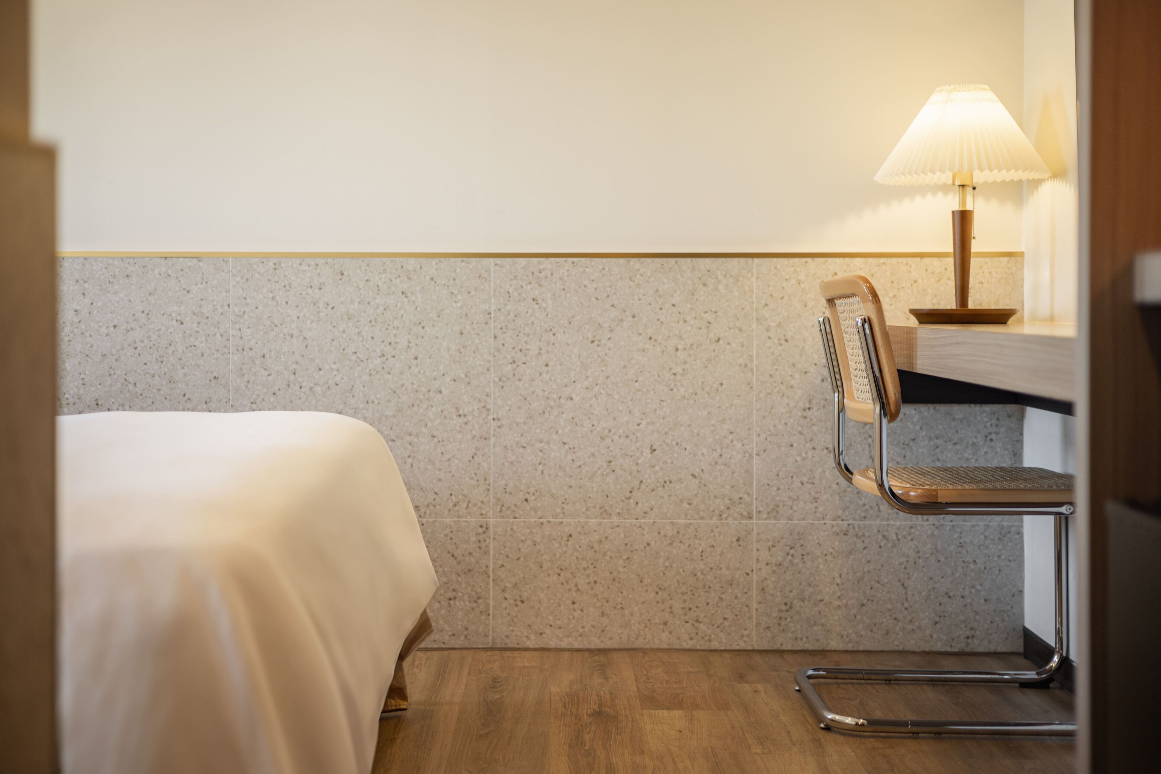 A hotel room with a bed, a chair, and a table with a lamp.