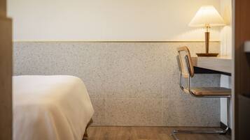A hotel room with a bed, a chair, and a table with a lamp.