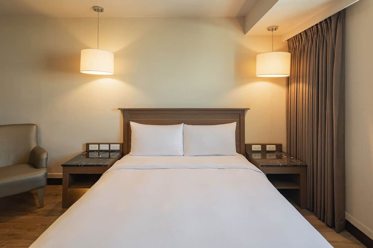 Ein Hotelzimmer mit einem großen Bett, zwei Nachttischen, einem Sessel und zwei Pendelleuchten.