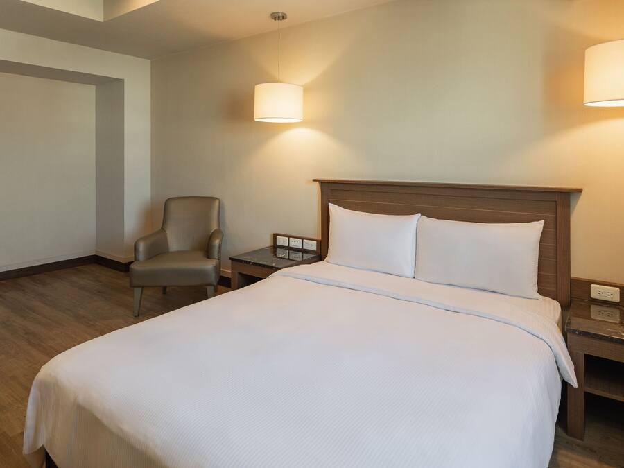 A hotel room with a large bed, a chair, a nightstand, and two wall-mounted lamps.