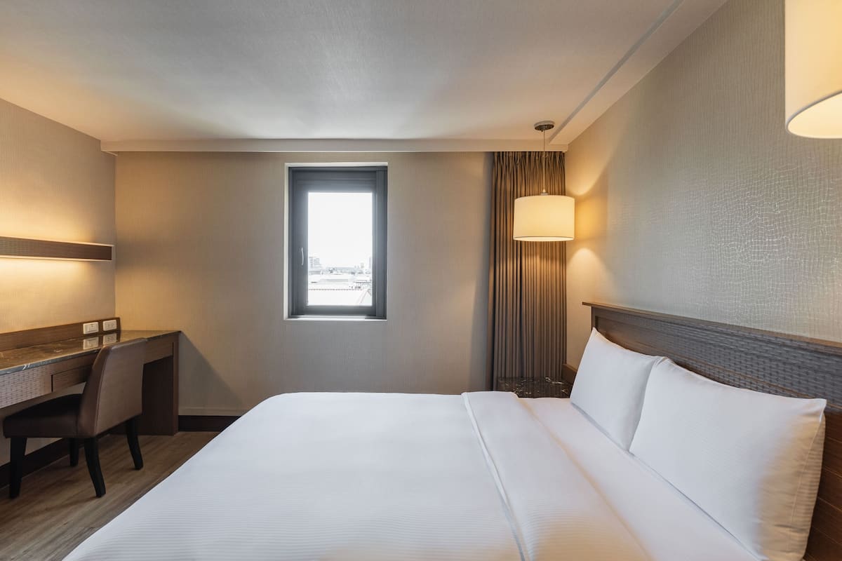 Ein Hotelzimmer mit Bett, Schreibtisch, Stuhl, Fenster und Lampe.