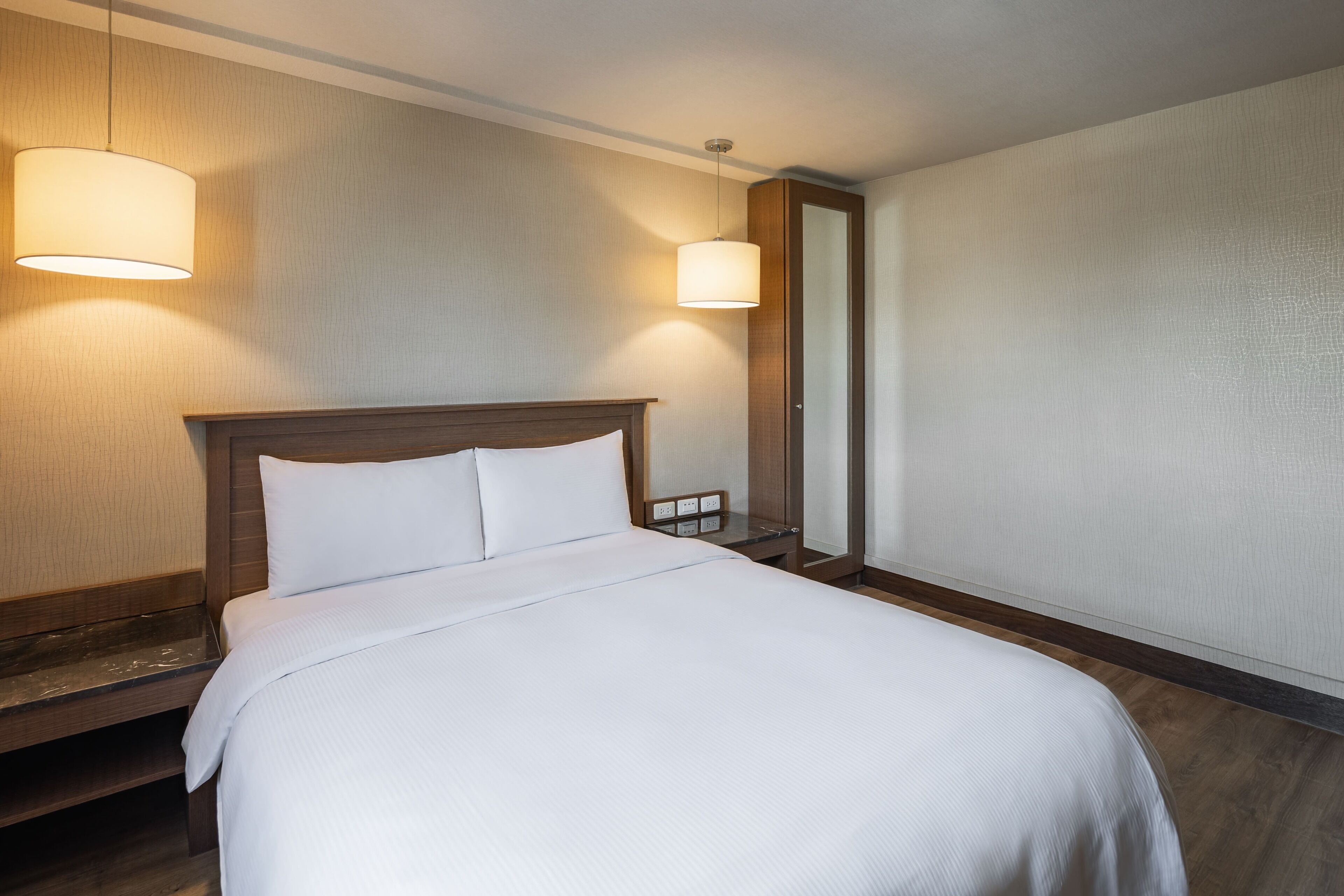 A hotel room with a large bed, two bedside lamps, a nightstand, and a mirror.