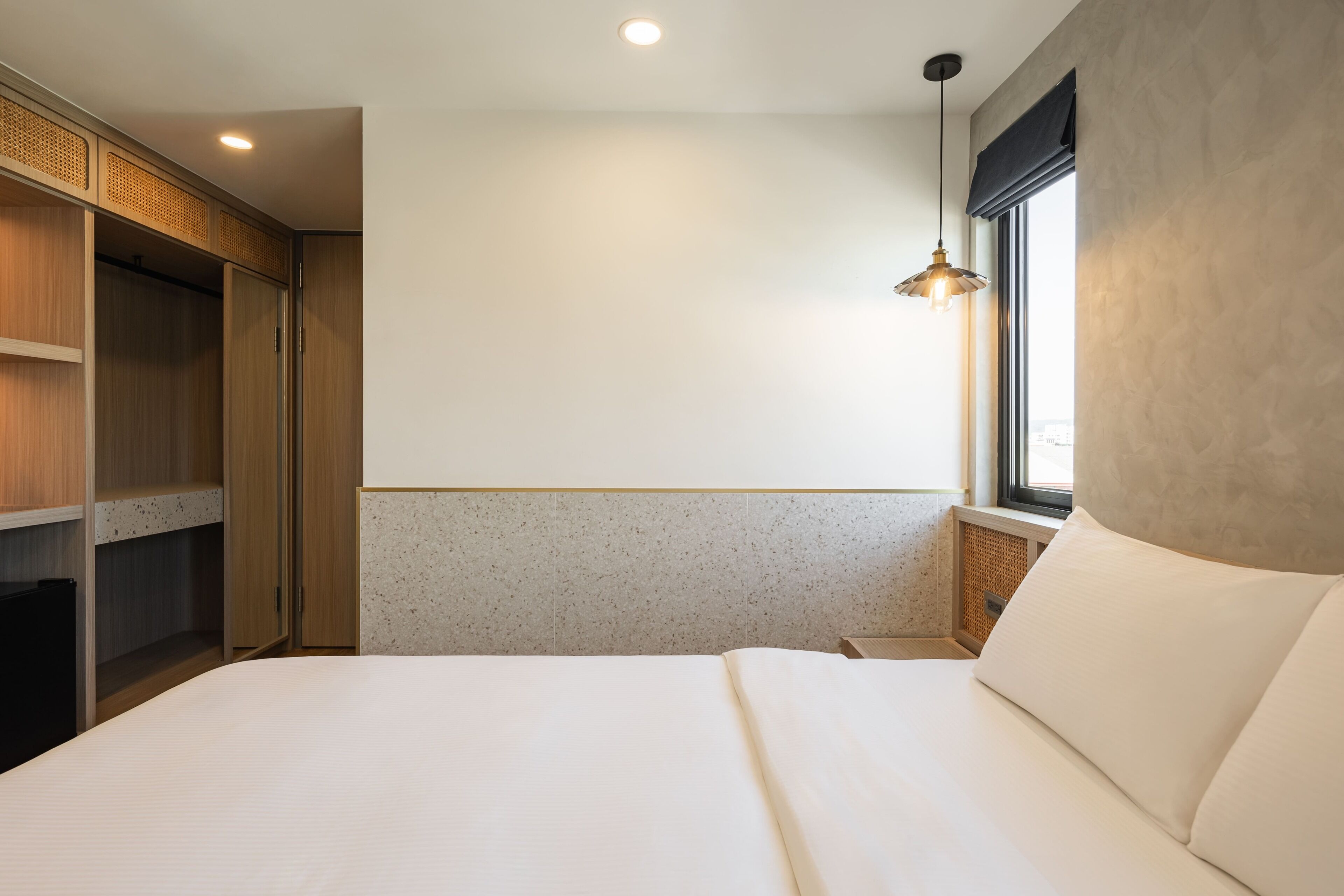 A bedroom with a bed, a wardrobe, a window with a view, and a hanging light fixture.
