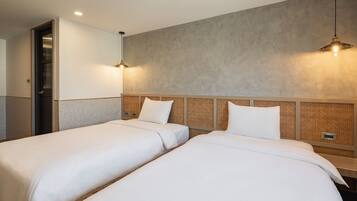 Habitación de hotel con dos camas individuales, cabecero de madera, pared texturizada e iluminación colgante.