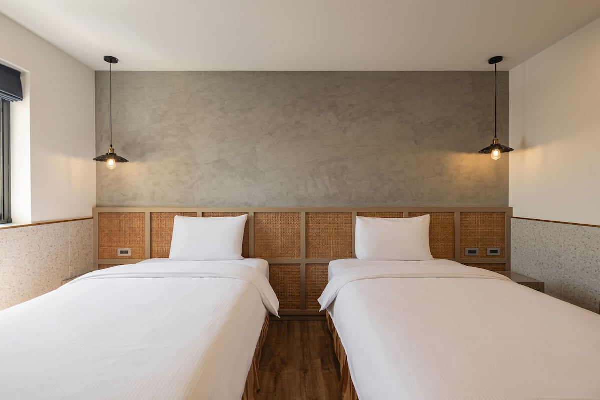 Ein Hotelzimmer mit zwei Einzelbetten, einer Betonwand, einem Holzkopfteil und zwei Pendelleuchten.