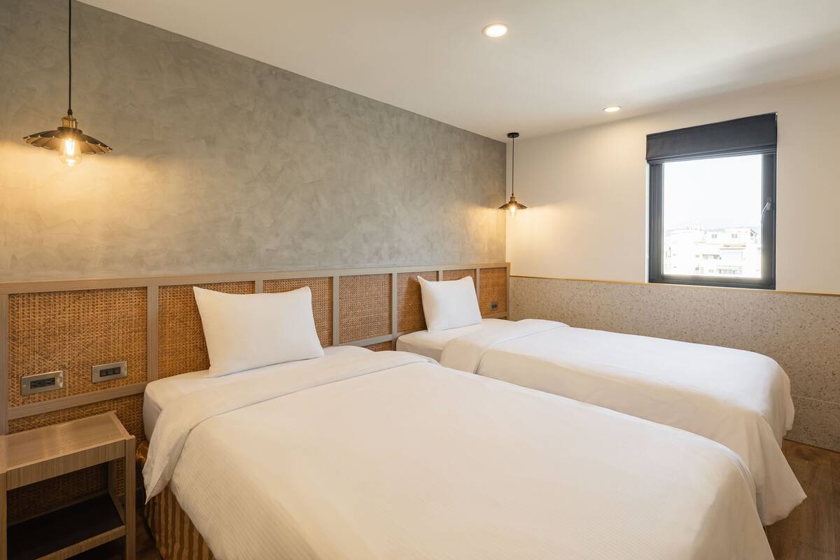 Ein Hotelzimmer mit zwei Betten, einem großen Fenster und einer strukturierten Wand.