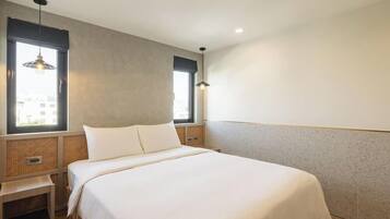 Une chambre à coucher avec un lit, deux fenêtres, une table de chevet et un luminaire suspendu.