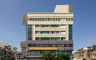 Un hotel de varios pisos con fachada moderna, que destaca un letrero del hotel y una unidad de aire acondicionado visible.