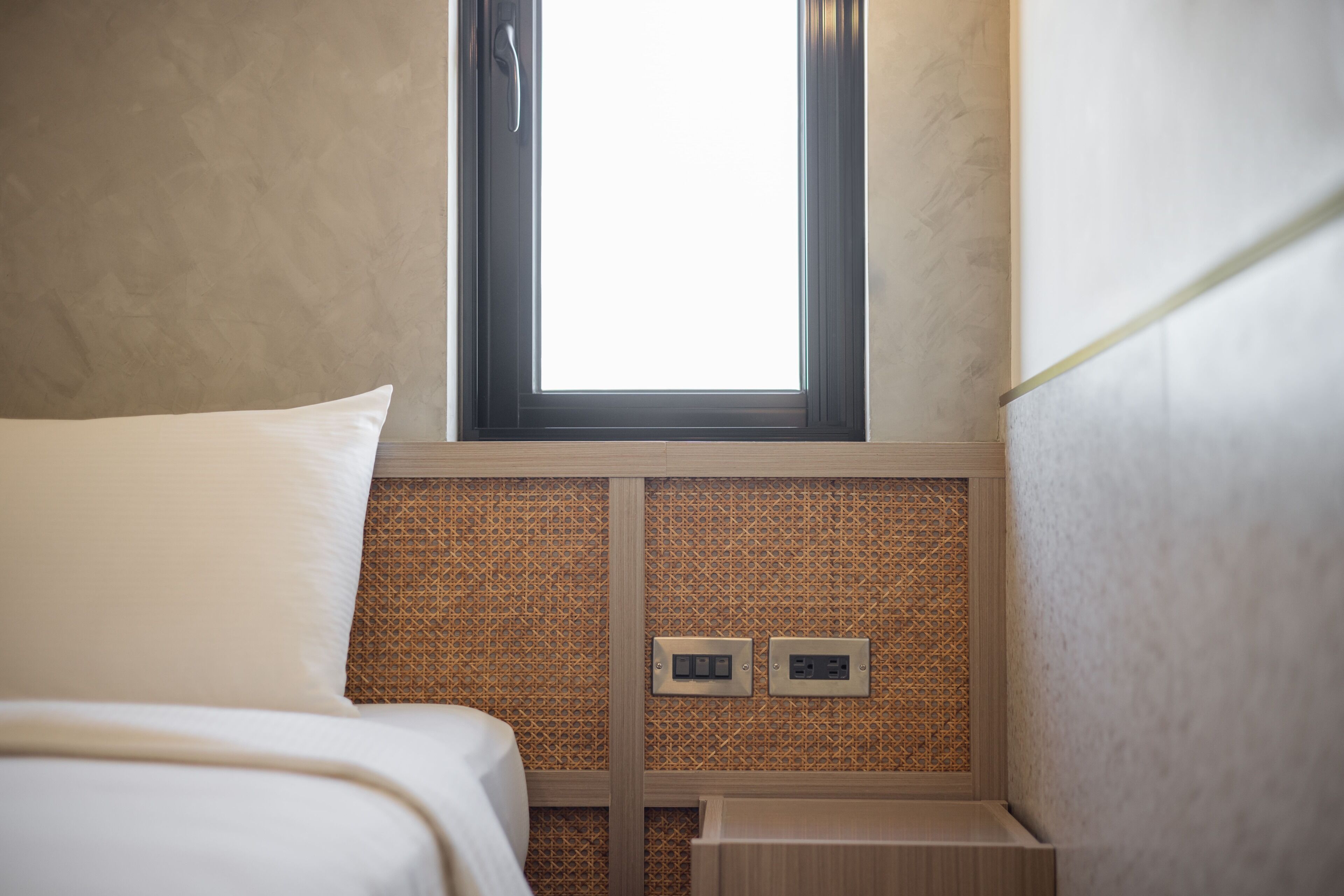 Une chambre d’hôtel avec un lit, une fenêtre et une prise électrique fixée au mur.