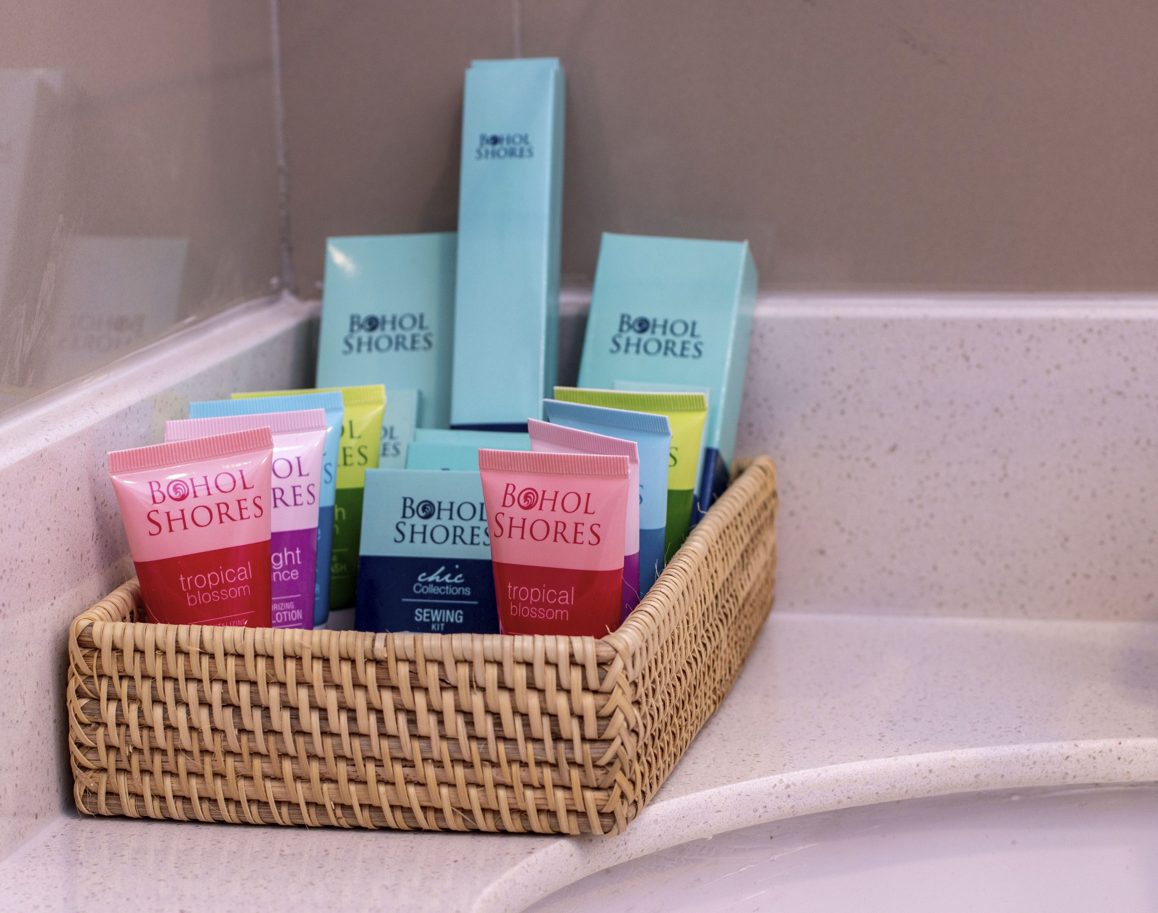 A wicker basket filled with various Bohol Shores products, including tubes and bottles, placed on a bathroom counter.