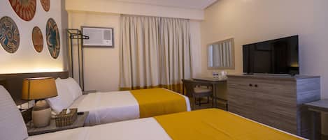 A hotel room with two beds, a desk, a television, and a wall-mounted air conditioner.