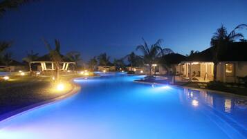 A swimming pool at dusk with surrounding palm trees and buildings.