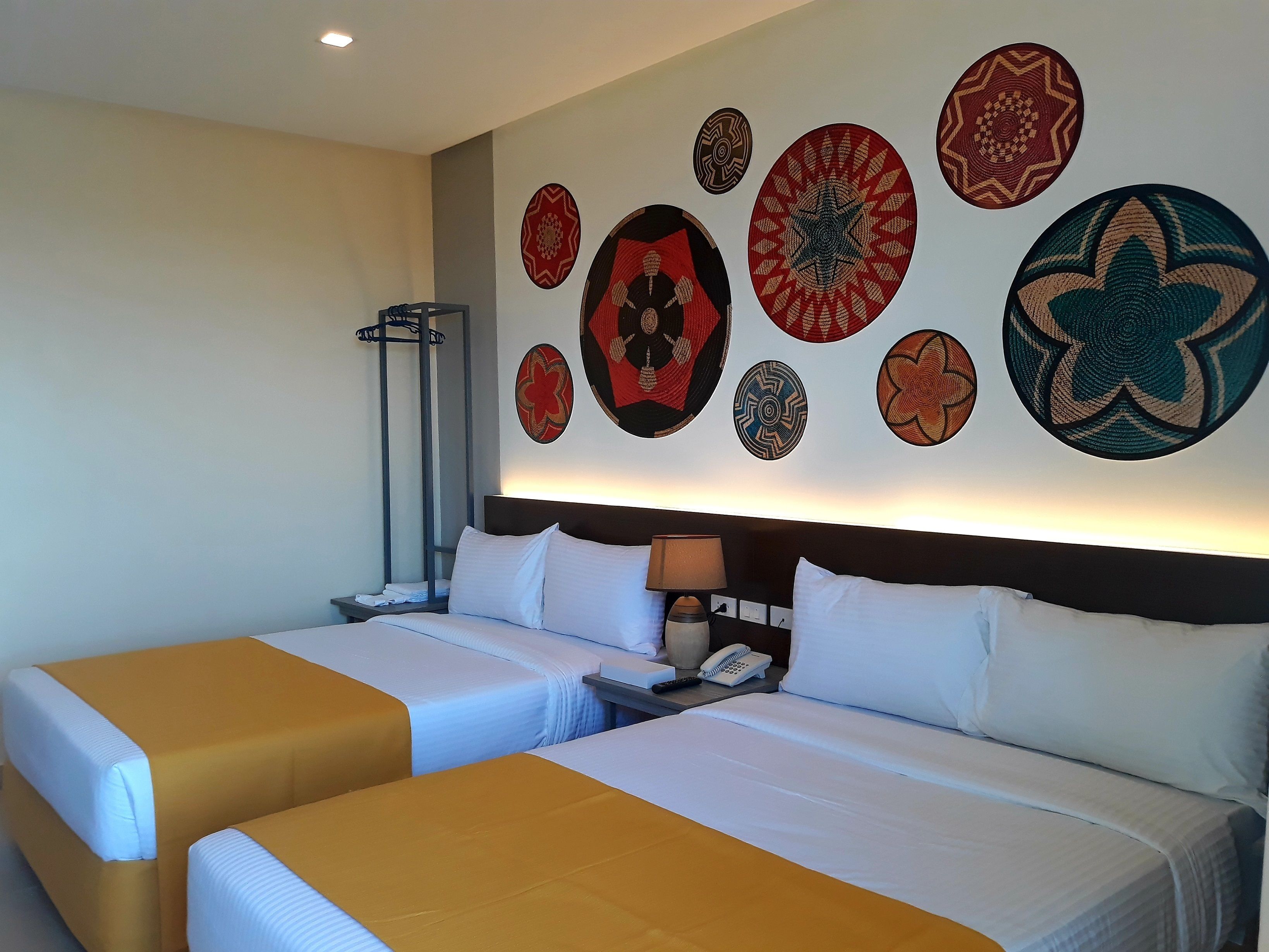 Una habitación de hotel con dos camas, una mesita de noche con lámpara, teléfono y decoración en la pared.