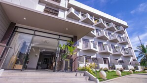 A modern hotel with a glass entrance, multiple balconies, and a well-maintained garden. - Bohol Shores (Dauis)